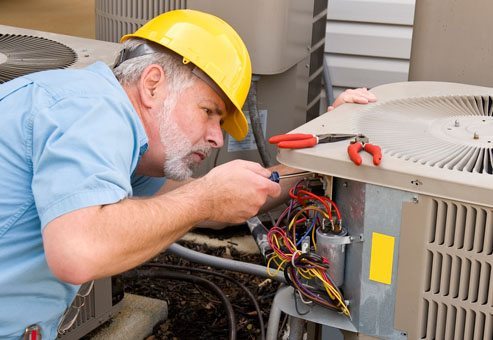 Technician repairing outdoor AC unit while wearing a yellow hard-hat.