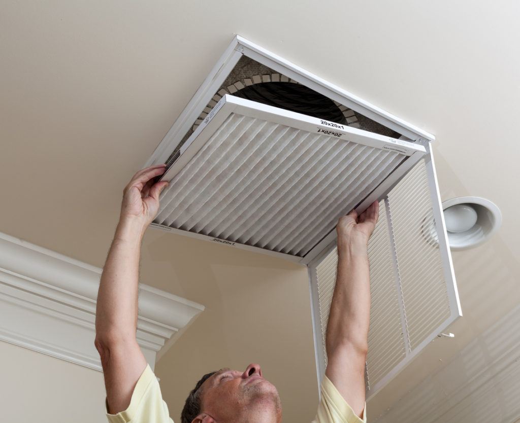 Senior male reaching up to open filter holder for air conditioning filter in ceiling