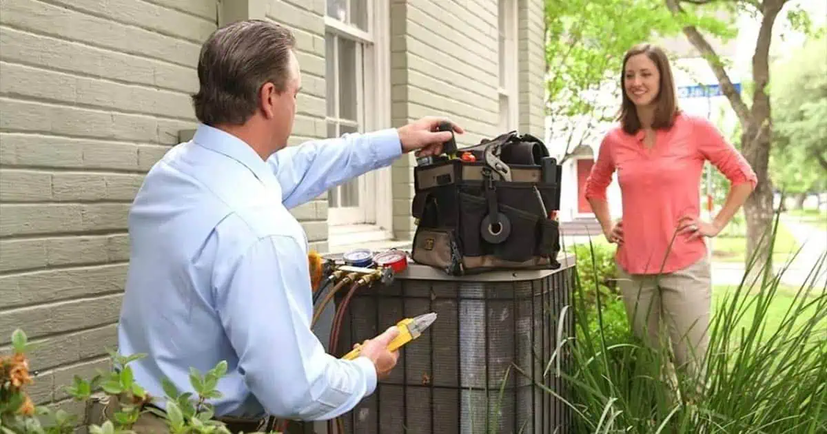 Homeowner standing outside next to repair technician working on AC condenser
