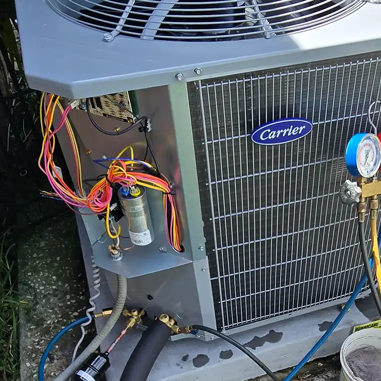 Open control panel of a Carrier outdoor AC unit showing electrical wiring, a capacitor, and connected manifold gauges during service.