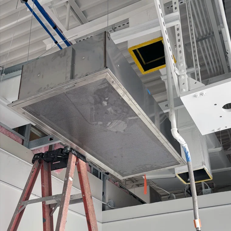 Suspended commercial ceiling HVAC air handler unit with a stepladder set up below for maintenance.